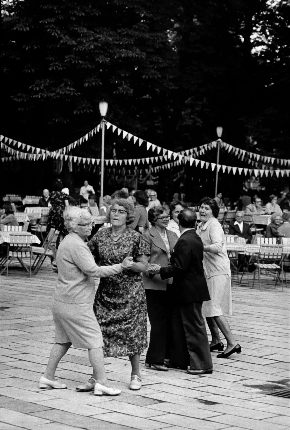 Im Pratergarten tanzen Senior:innenpaare. Im Hintergrund sind die Tische und Stühle des Biergartens zu sehen.